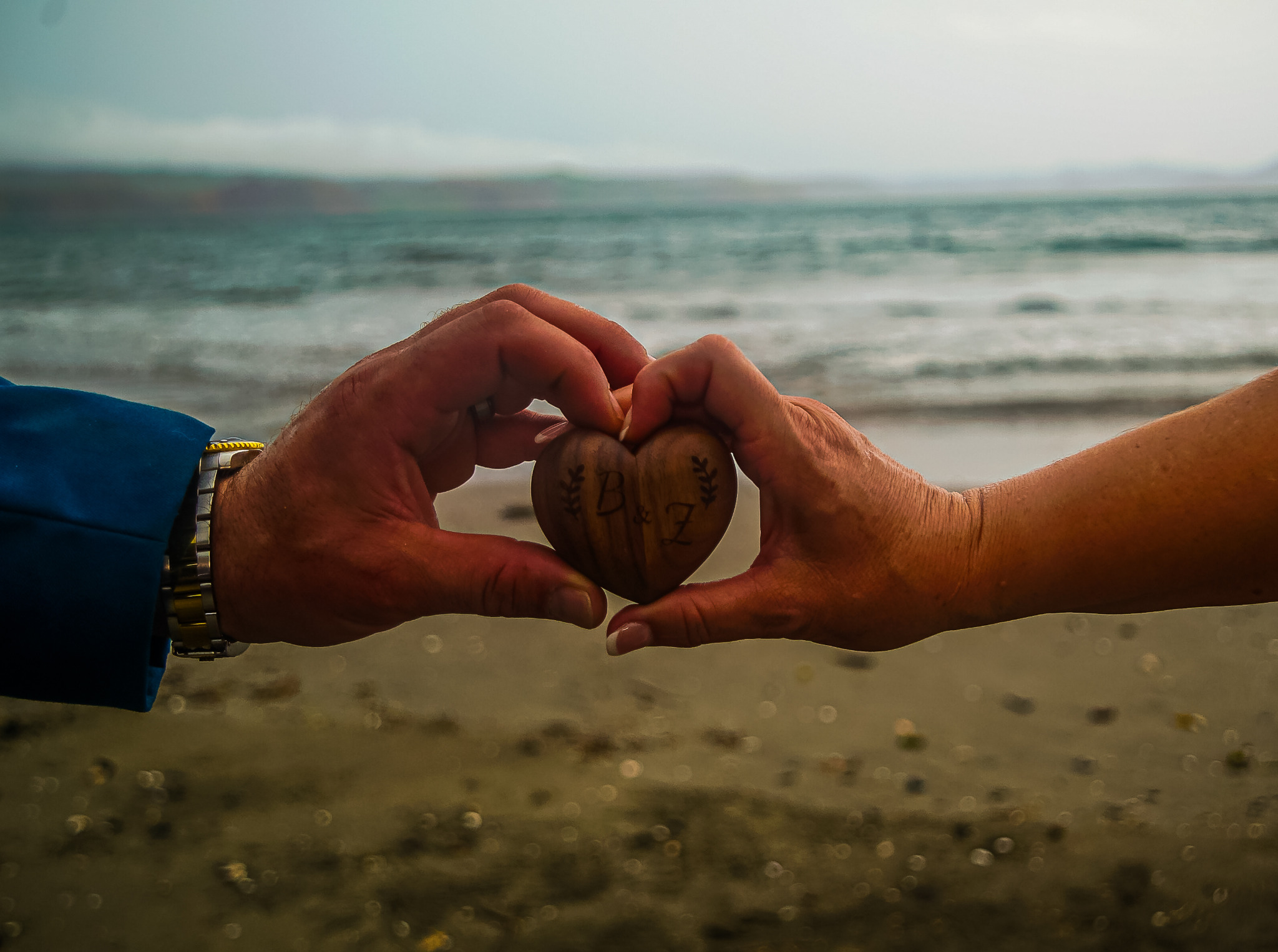 The couple holding a wooden B and Z heart by the ocean